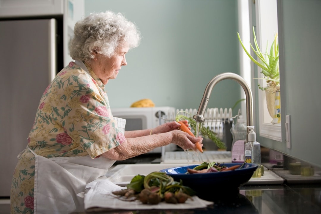Woman washing a carrot in a brightly lit kitchen.